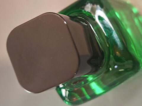 Close up view of a green glass cosmetic bottle with white cap, showing transparent packaging, beauty product design, skincare concept, modern minimal style and glossy glass texture.