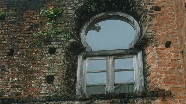 Weathered window with rounded arch set in red brick facade, overgrown plants on masonry of historical castle ruins, heritage architecture background for historical documentary or travel promo
