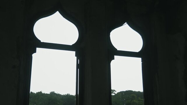 Antique arched windows looking out to nature, inside ancient medieval castle, silhouettes of ogee arches, dark stone room interior, historical heritage site, architectural detail