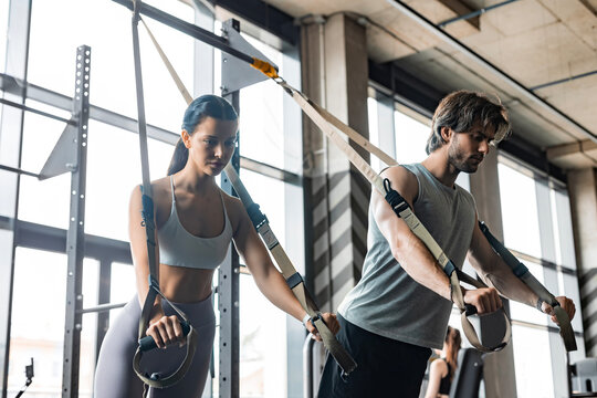 Young couple on body training with trx in gym.