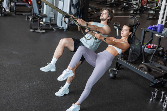 Young couple on body training with trx in gym.