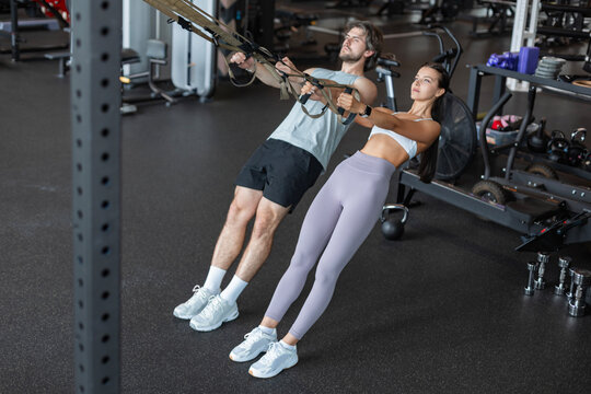 Young couple on body training with trx in gym.