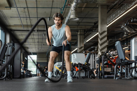 Athletic young man with battle rope doing exercise in functional training fitness gym.