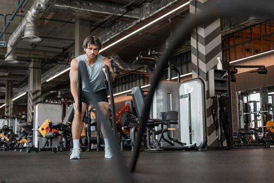Athletic young man with battle rope doing exercise in functional training fitness gym.