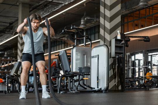 Athletic young man with battle rope doing exercise in functional training fitness gym.