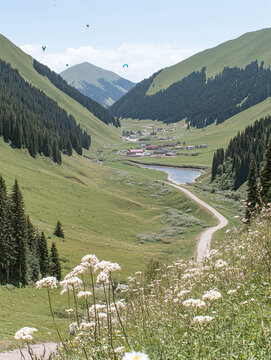 Beautiful green mountain valley with a winding road, small village, and river under a clear sky with paragliders