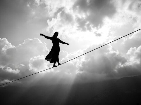 Silhouette of a Woman Balancing on a Tightrope Against a Dramatic Sky with Sun Rays