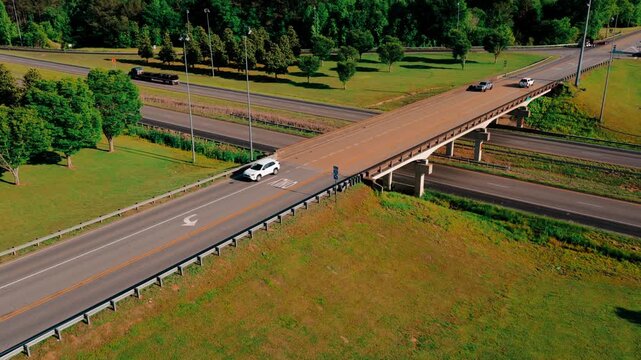 Semi truck hauling a tarped flatbed cargo load down a I-20 highway beneath an overpass, aerial drone freight transport shot, summer interstate, Heflin, Alabama, USA.