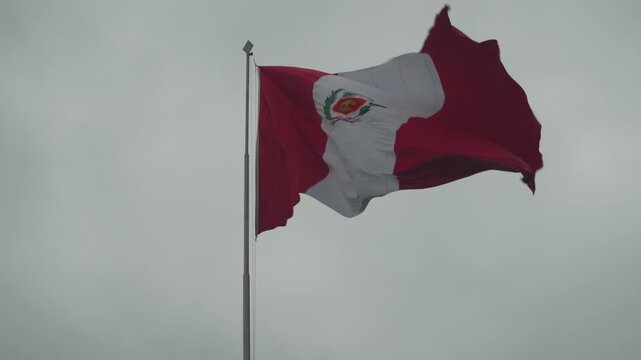 A very big Peruvian flag blowing in the wind. The camera stays still for a static shot. Recorded on a cloudy morning in a public park in Lima, Peru.