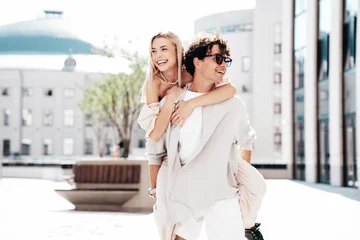Young smiling beautiful woman and her handsome boyfriend in casual summer clothes. Happy cheerful family. Couple posing in street at sunny day. Female sits at his back. piggyback riding © halayalex