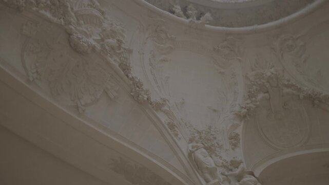 An upward view of an ornate vaulted ceiling decorated with gold detailing and classical sculptural elements inside a grand Parisian building.