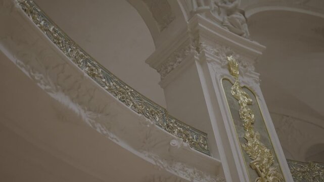 A close view of an elegant gilded spiral staircase railing inside a grand Parisian building, showcasing fine gold detailing against white stone.