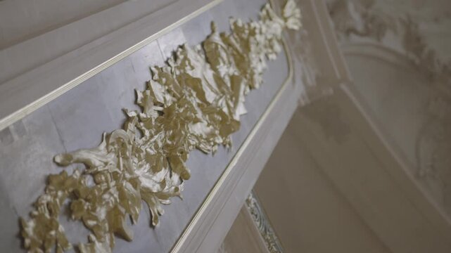 A macro close up of an intricate gold leaf ornament along the ceiling cornice of a grand Parisian interior.