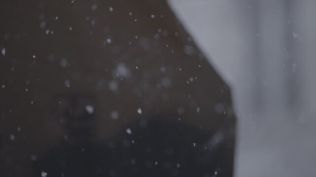 Snowflakes drift softly through frame with a blurred building facade behind, creating a delicate atmospheric winter texture shot for cutaways.