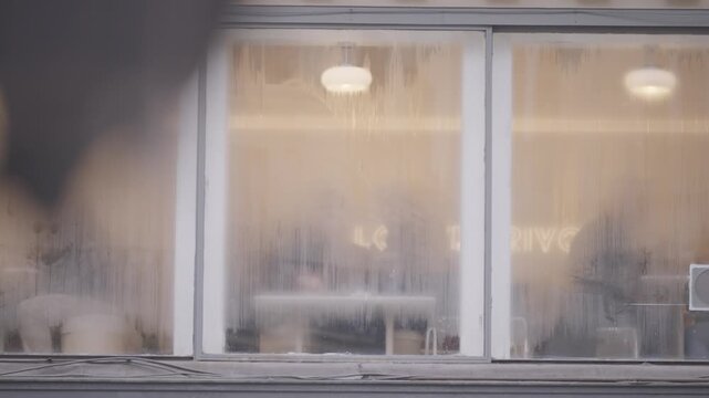 A frosted steamed up cafe window glows with warm interior light, blurring the scene inside on a cold Paris evening.