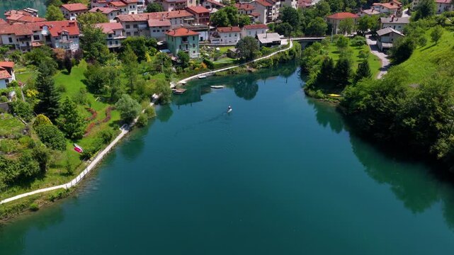 A man paddles across the calm lake in Most na Soci town, Slovenia, with tranquil water and the surrounding landscape visible - drone shot
