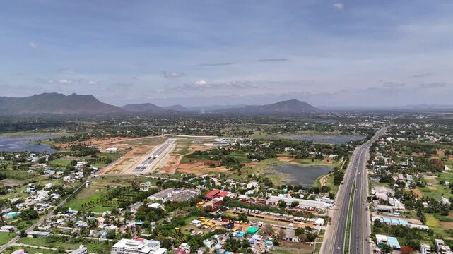Cinematic reverse drone footage retreating from an airport runway, uncovering a panoramic view of the city, highway, wetlands, and mountain horizon, green fields, scenic water bodies, and hills.