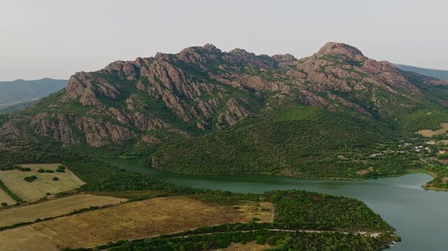 Scenic drone aerial of the rugged Monte Limbara mountain range rising above Coghinas Lake in northern Sardinia, Italy. Beautiful Mediterranean landscape with forests and rocky peaks.