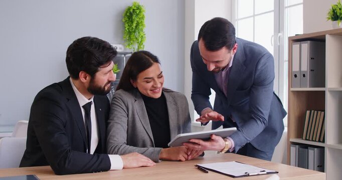 Couple as client engages in conversation or briefing with consultant or agent during office meeting, using tablet pc to discuss investment in a professional environment with focus and clarity.
