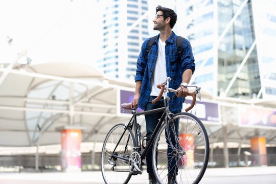Urban Commuter: Young man with beard stands with his vintage bicycle in front of modern buildings, enjoying a moment of reflection amidst the city bustle. Bike to work. Carbon footprint. Eco friendly 