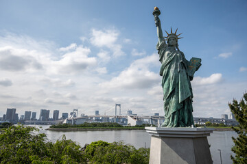 A replica of the Statue of Liberty stands in Odaiba, Tokyo, erected in 1998 after France lent a statue. The Rainbow Bridge and city buildings are visible. © Danica Chang