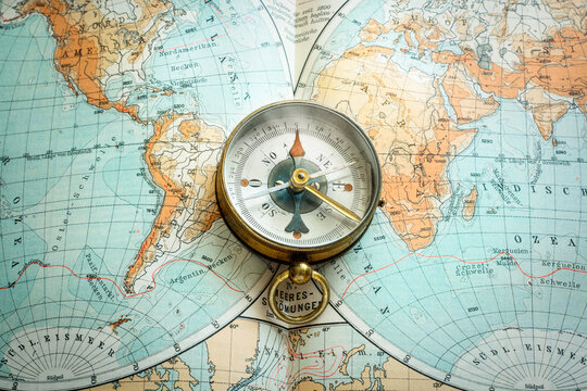 Vintage brass compass on an old geographic map close up. Antique navigation instrument for travel, exploration, geography and discovery concept.
