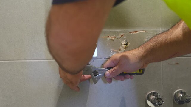 Plumber's hands using a wrench to mark where to drill holes in the tiled wall of the bathroom