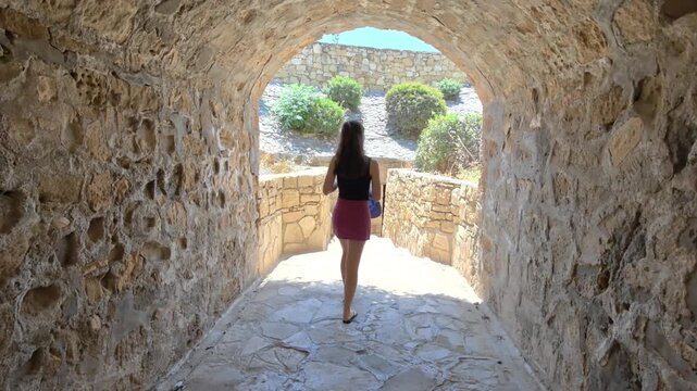 Young Woman Walking Through An Ancient Stone Tunnel Towards A Scenic Garden Exit On The Path To The Rock Of Aphrodite In Cyprus