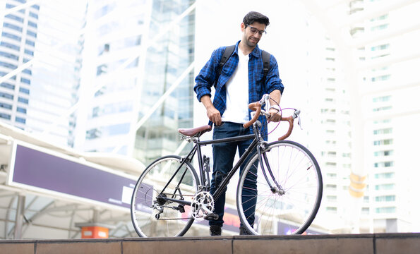 Urban Commuter: Young man with beard stands with his vintage bicycle in front of modern buildings, enjoying a moment of reflection amidst the city bustle. Bike to work. Carbon footprint. Eco friendly 