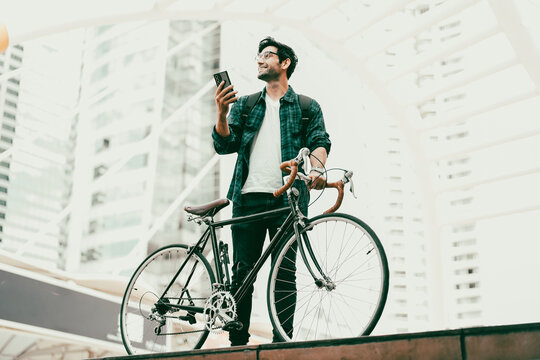 Urban Commuter: Young man with beard stands with his vintage bicycle in front of modern buildings, enjoying a moment of reflection amidst the city bustle. Bike to work. Carbon footprint. Eco friendly 