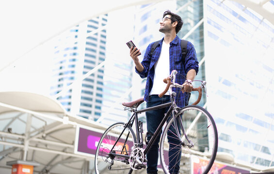 Urban Commuter: Young man with beard stands with his vintage bicycle in front of modern buildings, enjoying a moment of reflection amidst the city bustle. Bike to work. Carbon footprint. Eco friendly 