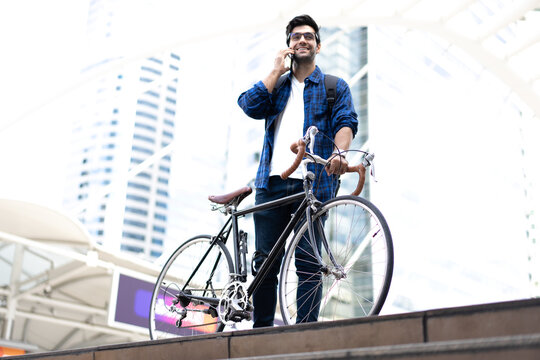 Urban Commuter: Young man with beard stands with his vintage bicycle in front of modern buildings, enjoying a moment of reflection amidst the city bustle. Bike to work. Carbon footprint. Eco friendly 