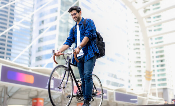 Urban Commuter: Young man with beard stands with his vintage bicycle in front of modern buildings, enjoying a moment of reflection amidst the city bustle. Bike to work. Carbon footprint. Eco friendly 