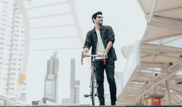 Urban Commuter: Young man with beard stands with his vintage bicycle in front of modern buildings, enjoying a moment of reflection amidst the city bustle. Bike to work. Carbon footprint. Eco friendly 