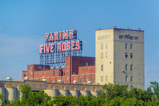Montreal, Quebec, Canada. July 26, 2026. Low angle shot of iconic Farine Five Roses neon sign atop industrial building against blue sky.