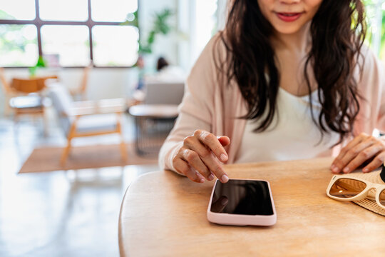 Close-up of a smiling woman swiping on a mobile phone screen on a wooden desk, cozy cafe background.