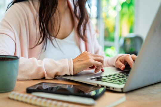 Cropped shot of a thoughtful Asian woman working on a laptop at a bright home desk