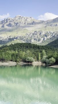 Majestic mountain peaks and billowing white clouds perfectly mirrored on the glassy surface of a secluded forest tarn