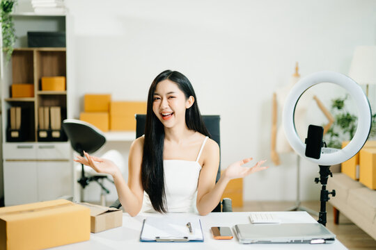 Beautiful Asian lady blogger showing clothes in front of the camera to recording vlog video live streaming at her shop.&nbsp;Online Shopping Cart notion.