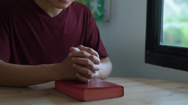 Faith and devotion concept. A man prays with his hands crossed over a Bible for God's blessing.  Spiritual devotion. Praying to God seeking solution to problems. Shot in 4k resolution.