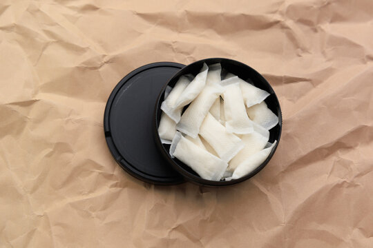 Snus pouches placed in a black container on brown paper background