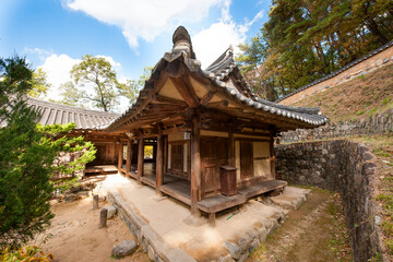 Obraz premium Traditional Korean Hanok Architecture and Courtyard Surrounded by Stone Walls and Trees under a Blue Sky
