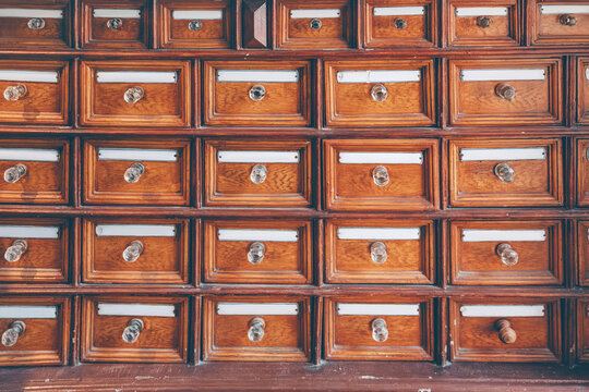 Old wooden file cabinet featuring many small drawers with glass knobs and label holders, symbolizing organization and archive