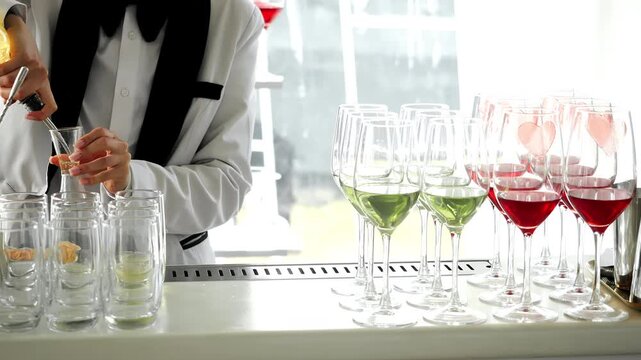Professional bartender prepares beverages behind a bar during a reception or catered event. Elegant drink service, glassware and hospitality concept for celebrations, restaurants and parties.
