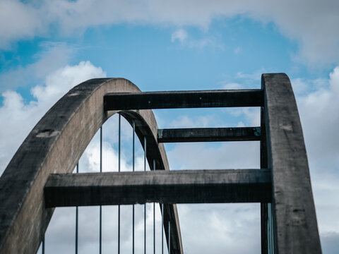 Low-angle view of the concrete arch bridge over the Purkijaur River in northern Sweden. Architectural perspective highlighting the bridge structure against a dramatic blue sky with clouds.