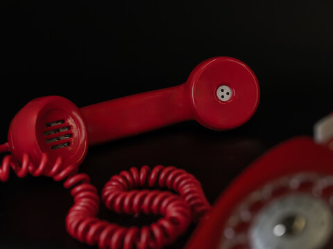 Vintage red rotary telephone handset with coiled cord on a black background.