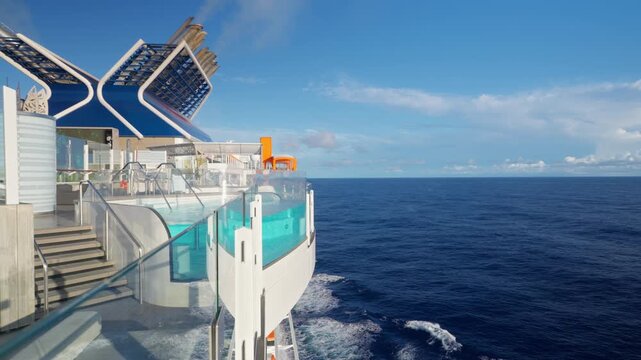 Cruise liner in Caribbean Sea featuring stunning infinity pool extending over ocean waves. Modern ship deck showcases glass railings and contemporary design under clear blue sky with scattered clouds.