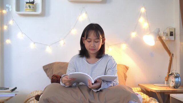 Happy young girl enjoys reading a book while sitting comfortably on bed in a warm and inviting bedroom	