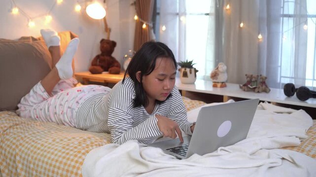 Young woman relaxing on a bed using a laptop, Workspace for Remote Learning in a cozy, softly lit bedroom decorated with fairy lights