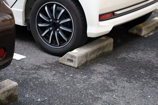 Car tire parked against a concrete wheel stop in an asphalt parking lot.